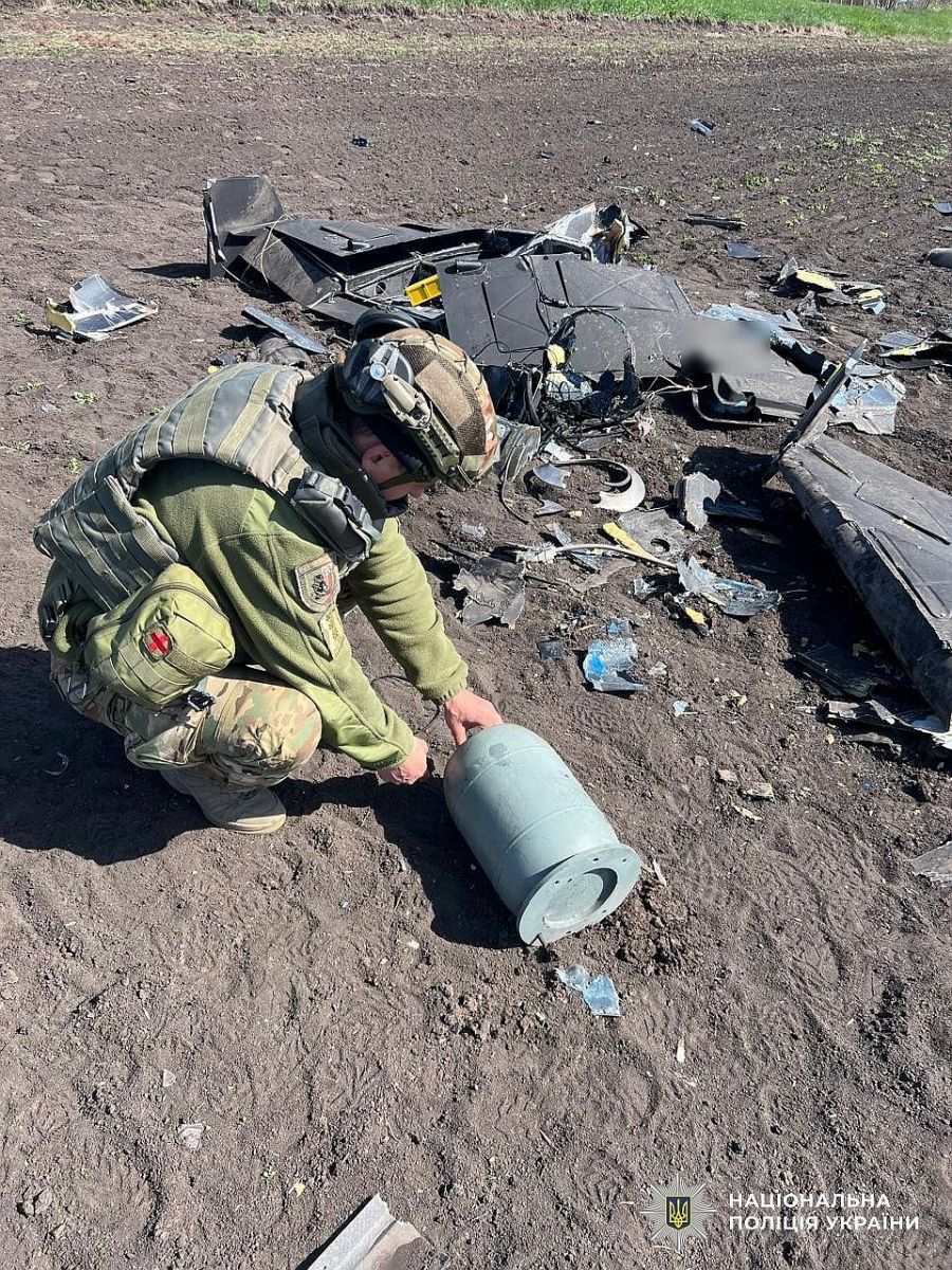 Фахівці вибухотехнічної служби поліції Кіровоградщини оглядають уламки збитого російського БпЛА на полі.