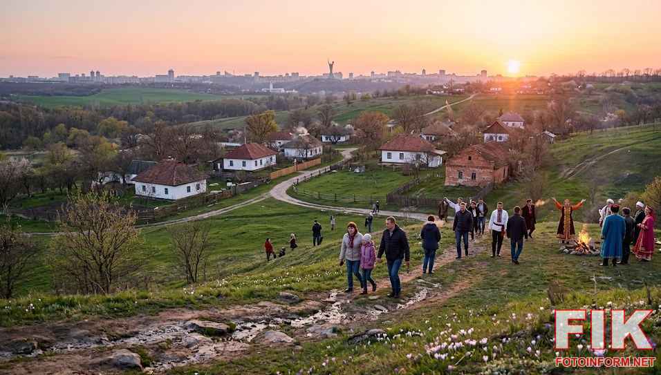 Весняне рівнодення та святкування Наврузу: люди біля вогнища на пагорбі на тлі панорами вечірнього Києва та квітучої природи.